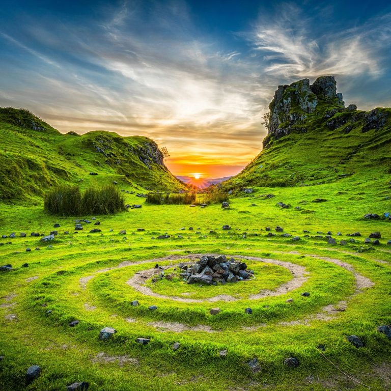 Kreisförmige Steinanlage in einer grünen Landschaft bei Sonnenuntergang.