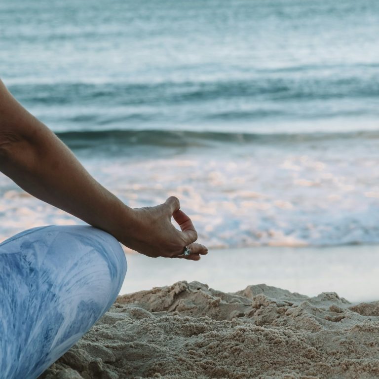 Eine Person in Meditationshaltung am Strand, mit Wellen im Hintergrund.