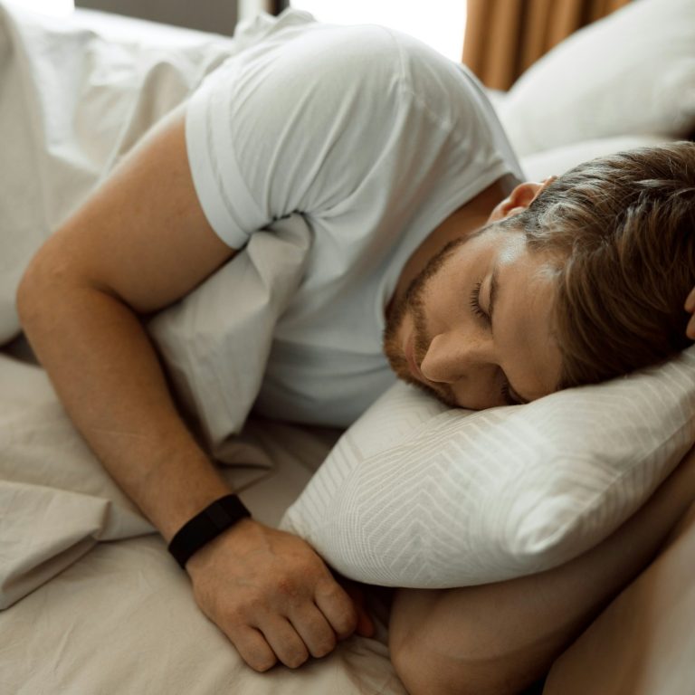 Mann schläft auf einem Bett, Kopf auf einem Kissen, entspannte Atmosphäre.